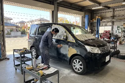 工場で黒いミニバンのパテを研ぐ作業